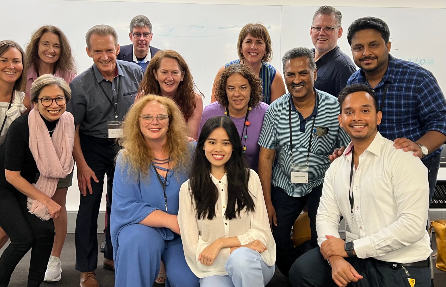 A group of fourteen smiling people huddled together for a group picture.